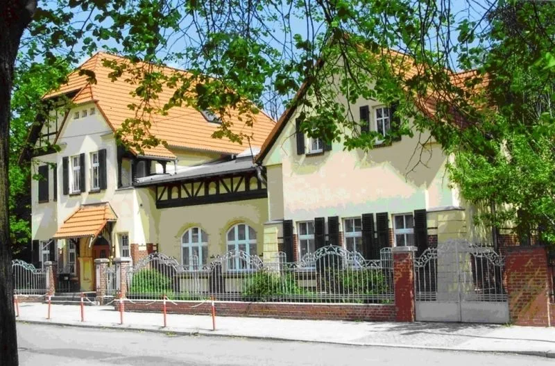 Die Marienschule von der Straße aus: helles Gebäude mit Fachwerkgiebel, Rundbogenfenstern und schmiedeeisernem Zaun.