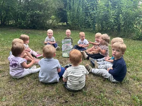 Kleine Kinder sitzen im Kreis auf der Wiese, in der Mitte steht ein Glas mit etwas zum Beobachten.
